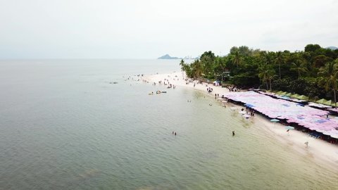 Aerial view of the sandy beach with green tropical palms, surrounded by ocean in Hua Hin, Prachuap Khiri Khan Province, Thailand