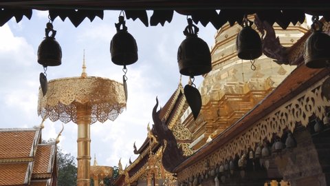 Row of small temple bells hanging from the eaves with background of gold plated chedi and buildings at Wat Phra That Doi Suthep, one of the most famous Buddhist temple in Chiang Mai, Thailand.