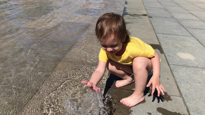 Caucasian toddler girl in yellow t-shirt plays with water and squirts. Summer 