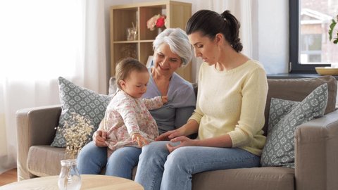 family, generation and female concept - mother, daughter and grandmother sitting on sofa at home