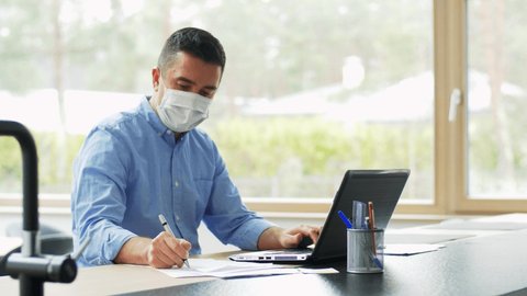 quarantine, remote job and pandemic concept - middle-aged man wearing face protective medical mask for protection from virus disease with laptop computer working at home office