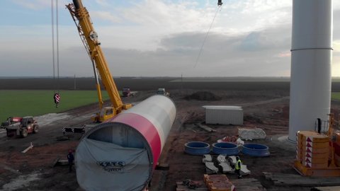 Building process of wind energy power tower, windmill under construction. Transportation of tower part, assembling the pillar. Green, clean, renewable energy. Aerial footage.