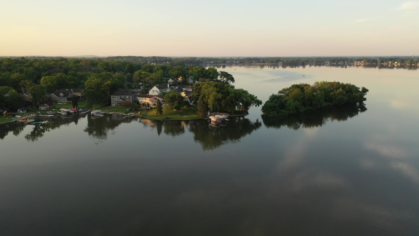 Aerial view of american suburb at summertime.  Establishing shot of american neighborhood. Real estate, residential houses with boat launch on the lake shore. Drone shot, from above, sunrise, morning