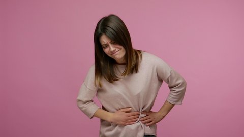 Gastrointestinal disease. Woman suffering intense abdominal pain, frowning from stomachache, painful cramps of indigestion, constipation, period spasms. indoor studio shot isolated on pink background