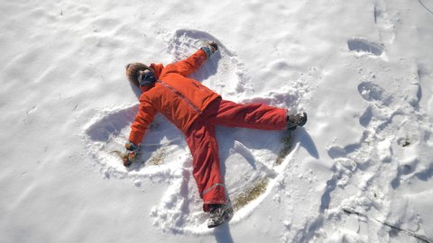 One child lies on ground and makes snow angel, winter fun