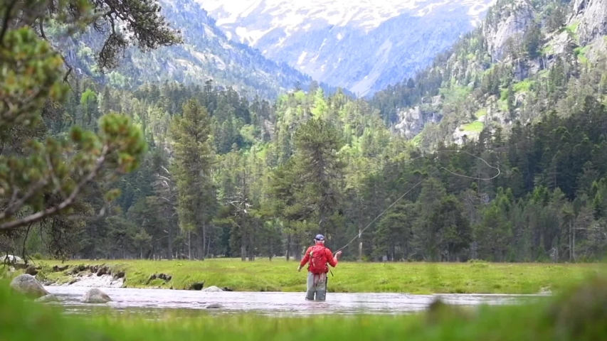 fly fisherman trout fishing with a hiking backpack and an orange jacket in the high mountains in summer