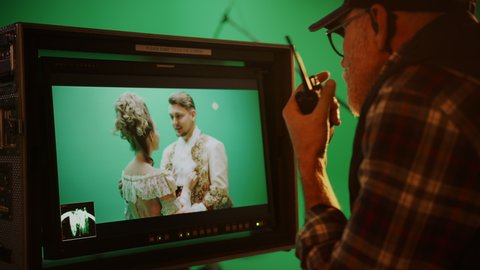 Director Looks at Display Controls Shooting Period Drama Movie. Green Screen CGI Scene with Actors Wearing Renaissance Costumes. Big Film Studio Professional Crew Shooting High Budget Movie. Side View