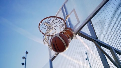 Brown basketball ball fall through basket with net on sunny summer day close up on background of clear blue sky. Concept of modern urban playing field. Slow motion