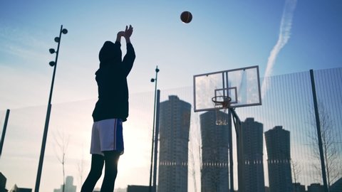 Back view of unrecognizable player throwing ball in a basketball hoop, the ball hits the ring and scores. Slowmotion shot