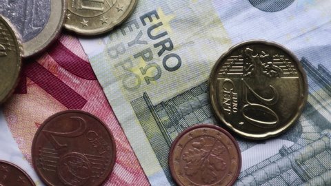 Euro banknotes and coins rotate as background. Shot looking down on a euro currency rotating. Coins are stacked on top of each other in different positions. Money concept.