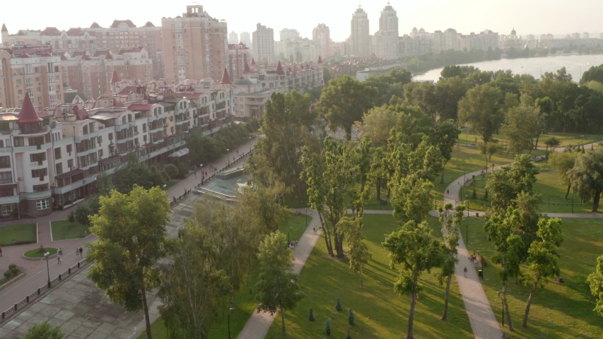 Aerial view. High-rise buildings with residential apartments and shops in a big city with green trees. People are walking near the city park in Kiev, Ukraine