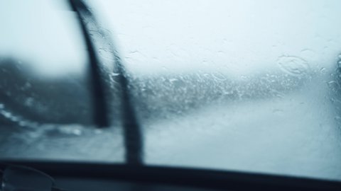 Front car windshield with rain drops on it while driving. Focusing rain drops. Driving in the rain.