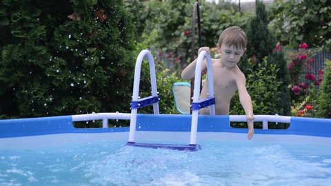 Summer holidays during quarantine. Boy at the pool playing with water. Outdoors home pool.