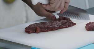 Professional male chef cutting fresh meat at kitchen board, close up