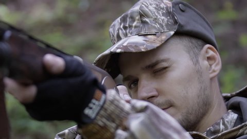 Portrait of hunter takes aim from hunting rifle. Man in comfortable camouflage clothes hunts outdoor in forest hunting alone. Hunter in camouflage aims gun at object in forest.