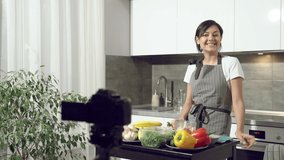 Attractive young woman recording a video about healthy eating on digital camera in the kitchen at home. Vlogging and social media concept.