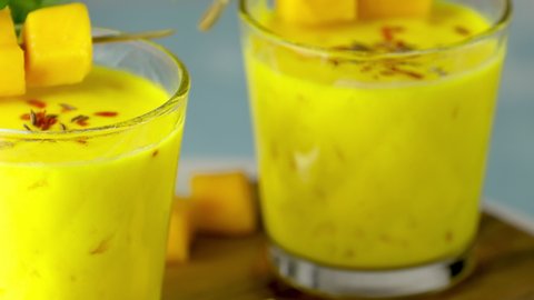 Yellow Indian mango yogurt drink Mango Lassi or smoothie with turmeric and saffron. Healthy probiotic Indian cold summer drink moving slowly on blue background