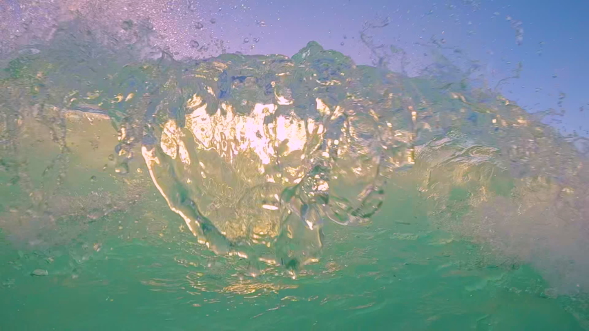 SLOW MOTION UNDERWATER, LENS FLARE: Crystal clear ocean wave breaking over the camera at golden sunset in the Caribbean. Cinematic shot of a tube wave splashing over camera filming the summer sunset.