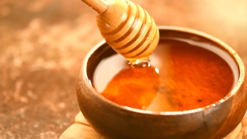 Honey dripping, pouring from honey dipper in wooden bowl.  Close-up. Healthy organic Thick honey dipping from the wooden honey spoon, closeup. 4K UHD video footage. Slow motion. 