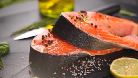 Salmon fish. Raw Trout Red Fish Steak with Herbs and Lemon and olive oil rotation, on slate. Cooking fresh salmon, sea food. Healthy eating concept. Slow motion 4K UHD video