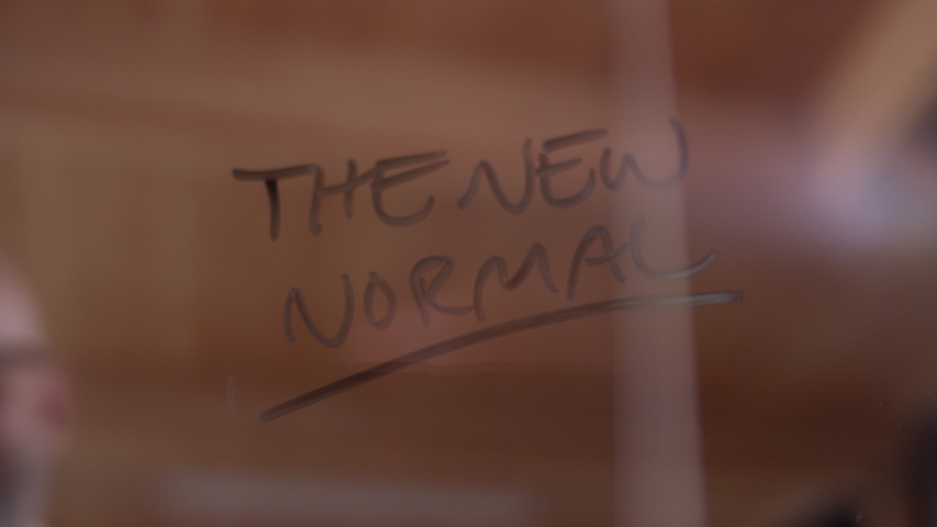 "The New Normal" getting erased on clear glass by a modern businessman