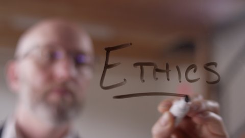 "Ethics" written on clear plexiglass with a dry erase marker by a modern businessman