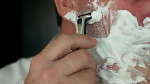 Caucasian man shaves his face with a classic razor with a blade and foam close-up 