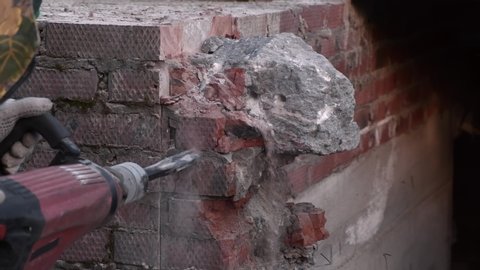 Worker breaks concrete at a construction site. Powerful hammer drill breaks brick and concrete. Slow-motion.