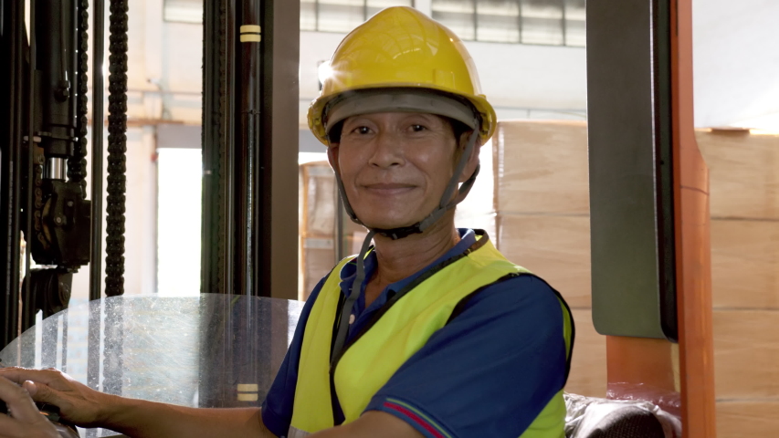 Portrait of happy asian old man labor looking at camera , smie and sitting on forklift with light of spotlight warehouse background. Adult male worker yellow helmet feeling confident and smilling. Royalty-Free Stock Footage #1054778093