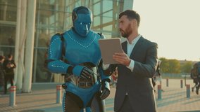 Slow motion young man use tablet computer talking with humanoid robot shows the way digital future in the city virtual intelligence smart communication close up outdoors