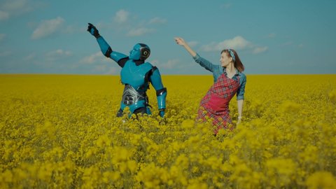 Funny cyborg android robot dancing in couple with young cheerful pretty woman romantic dance on yellow flower field outside. Human and robots friendship.