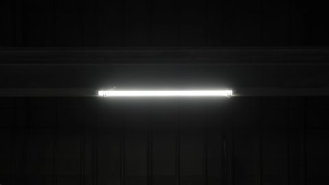 Led light lamp on metal beam partition blinks and turns on in dark room of plant, hangar, workshop department without windows. Power failure, electrical short circuit in industrial manufacturing area