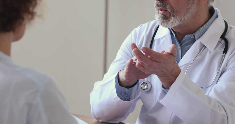 Close up focused senior male therapist gesturing, giving healthcare advice to young woman. Female patient listening to older senior doctor explaining treatment during checkup visit in clinic office. | Shutterstock HD Video #1054786331