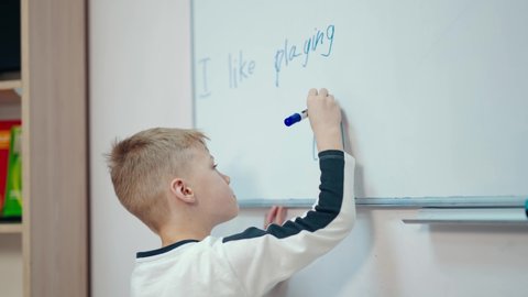 Schoolboy near the whiteboard. Happy boy drawing with a marker on a board in the classroom. Primary pupil at school.