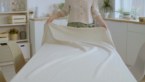 Medium shot of unrecognizable woman laying beautiful beige tablecloth on dining table Video de stock