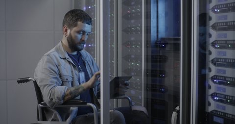 Medium shot of a wheelchaired technician engineer checking servers in data center