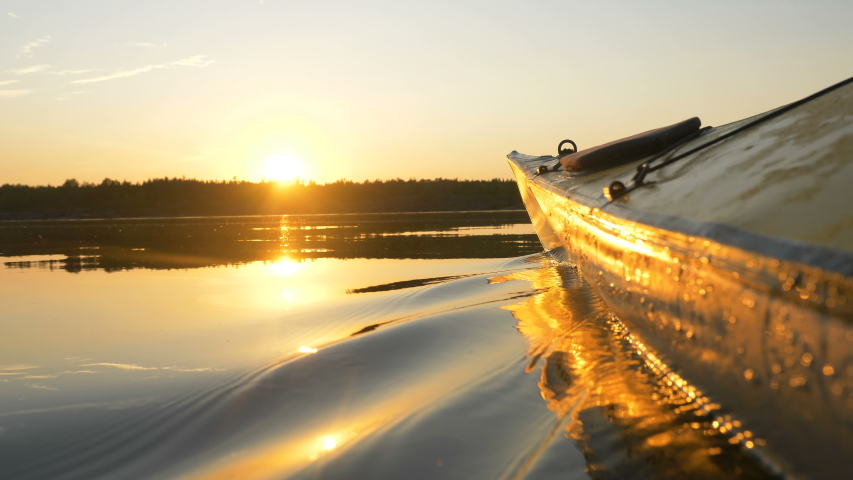 Rubber boat kayak nose cuts the surface of the water at sunset on the lake, outdoor activities