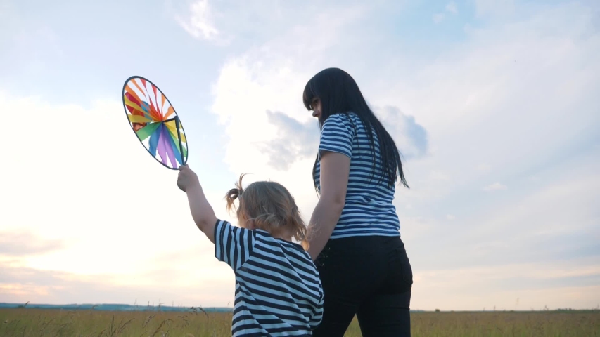Happy family. A mother with a lovely daughter walking on a green field. In the hands of a child, a toy for the wind.