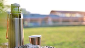 Video of a thermos in the evening sun on a background of a landscape without people. Shot in summer in clear weather. Tourist vacation concept.