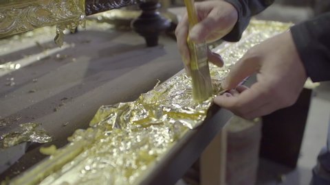 Artisan gildes furniture using golden paper and brush, slow motion
