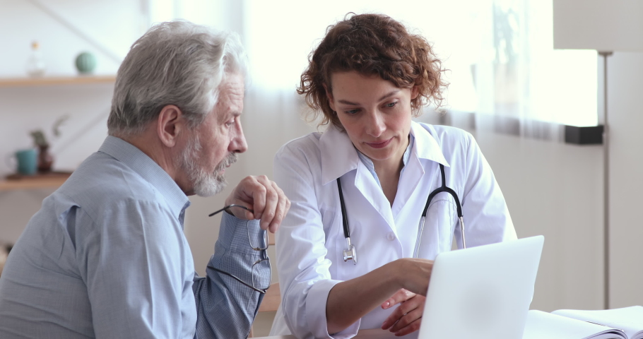 Serious young female doctor in medical uniform consulting elderly male patient, showing lab test results on computer screen at checkup visit in hospital. Focused old man listening to cardiologist. | Shutterstock HD Video #1054798394