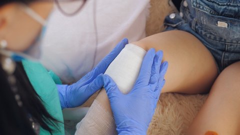 home doctor puts a bandage on the patient's knee with an elastic tubular mesh.
