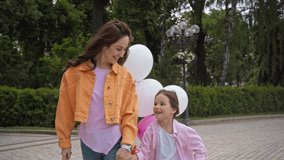 cute kid talking and holding hands with mother near balloons in park