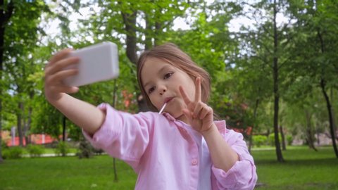 kid with lollipop taking selfie and showing peace sign in park