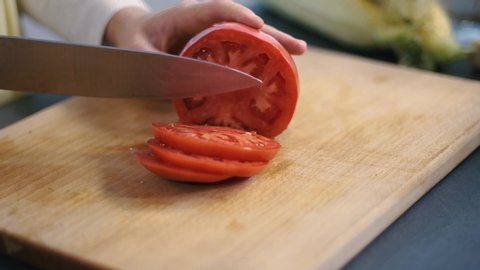 woman's hands using kitchen knife cutting fresh tomato on wooden cutting board. Healthy eating. Sliced tomato.