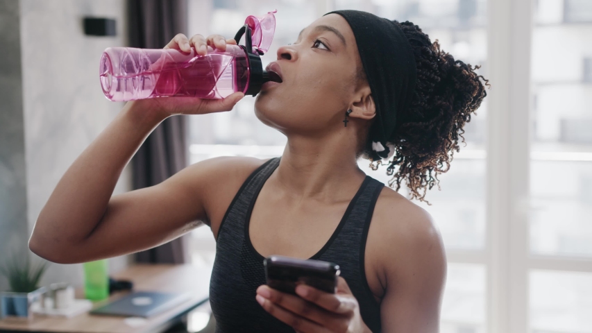 Portrait of charming african american woman in sport clothes lying on exercise mat after sports training, browsing social media content online on cellphone in domestic room, expressing positivity. Royalty-Free Stock Footage #1054807346