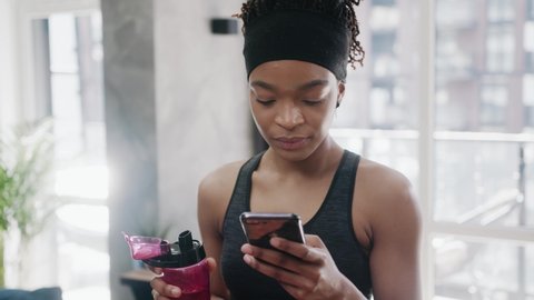 Portrait of charming african american woman in sport clothes lying on exercise mat after sports training, browsing social media content online on cellphone in domestic room, expressing positivity.