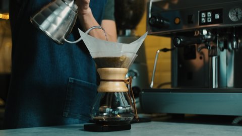 Barista making  Filter coffee by spilling hot water through a layer of ground coffee on the filter. Trendy drink brewed coffee dripping into a glass coffee pot.
