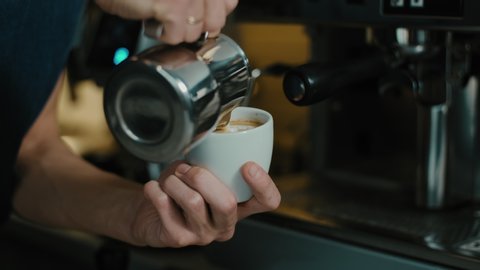 Barista making latte art in  specialty coffee shop. Professional man making pouring stream milk with espresso

