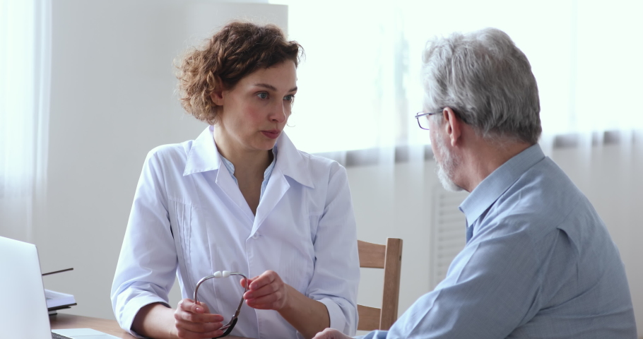 Focused young female cardiologist listening heartbeat of old senior male patient at checkup meeting in clinic office. Skilled 30s woman doctor checking lungs of mature middle aged man in hospital. | Shutterstock HD Video #1054810277